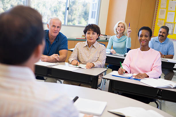 Mature female student raising hand in class Mature female student sitting in classroom raising hand middle age adult studying stock pictures, royalty-free photos & images
