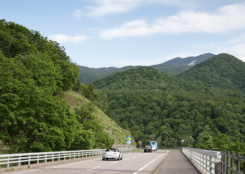 Shiretoko Peninsula, Japan - June 1, 2023: Traffic goes through Shiretoko  Peninsula on a spring afternoon. Blue skies with light clouds above the dense forests in eastern Hokkaido Prefecture.