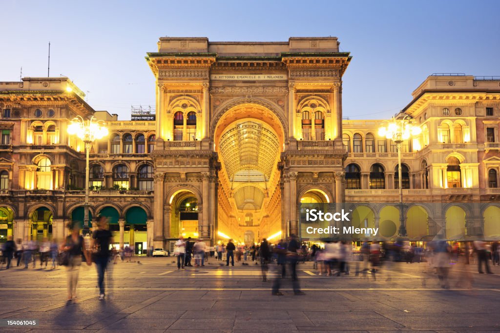 Galleria Vittorio Emanuele presso Piazza del Duomo Milan Italy Galleria Vittorio Emanuele II at Piazza del Duomo in Milan, Italy, the famous luxury shopping mall. Night Scene with illuminated building, long exposure, unrecognizable motion blurred people rushing through. Milan Stock Photo