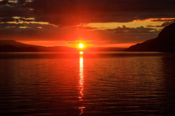 Sunset over water with mountain range in distance.