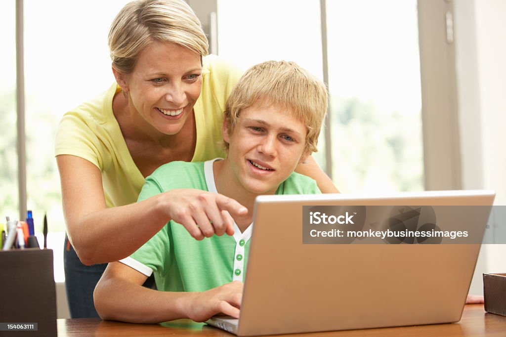 Mother helping her teenage son on the laptop Mother And Teenage Son Using Laptop At Home And Smiling 30-39 Years Stock Photo