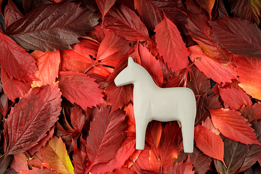 a gray toy horse is located on a surface of red leaves. dullness and red color of autumn