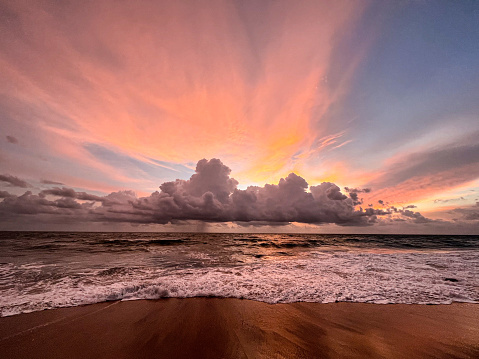 Sunset on the ocean with purple, orange and blue lights colouring the sky. Monsoon clouds surrounding golden setting sun. Far away it's raining at the horizon. Wide shot. Copy space, wallpaper, dream