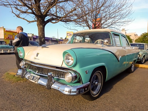 Buenos Aires, Argentina – May 29, 2023: An old white and aqua 1955 Ford Fairlane V8 four door sedan in a parking lot. Classic car show. Sunny day