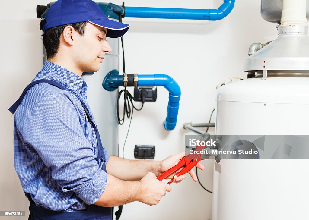 Worker repairing hot water heater with red wrench Smiling technician repairing an hot-water heater Boiler Stock Photo