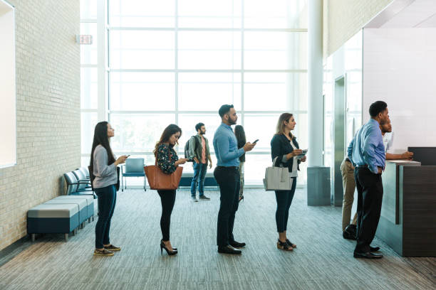 Customers with phones wait in line to see bank teller Diverse customers with phones in their hands wait in line to get their bank business done. waiting in line stock pictures, royalty-free photos & images