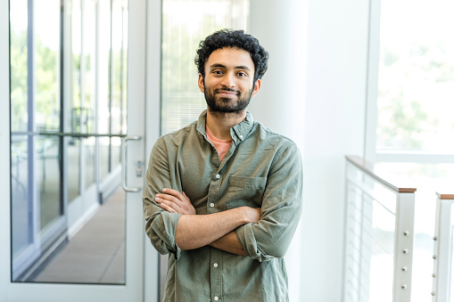 The young adult male design professional stands with his arms crossed as he smiles for the camera.