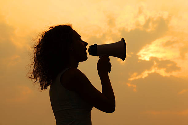 Woman holding megaphone and shouted into it at sunset stock photo