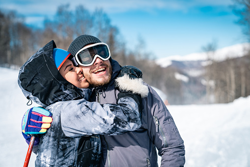 Young skiing couple enjoying their time in the mountains. Male and female skier feeling affectionate and joyful on ski slope in winter.