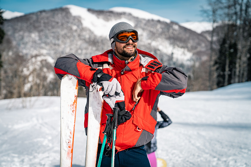 Smiling male skier enjoying the moment. Athletic happy man admiring the mountain range covered with snow during winter vacation.