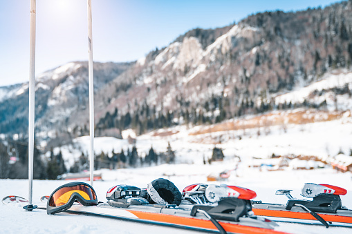 Close up of skis, ski goggles, ski gloves and ski poles. Sports equipment displayed in snow with magnificent mountains in the background.