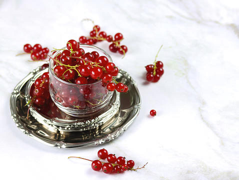 Ripe red currant berries in a transparent bowl on a marble table. Fresh red currants on light background with copy space. Atmospheric photo of red currants in rustic style. Selective focus.