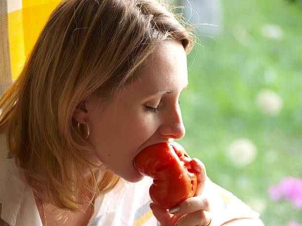 Blue pyjamas black hair little girl bitting a piece of the red tomato at the breakfeast