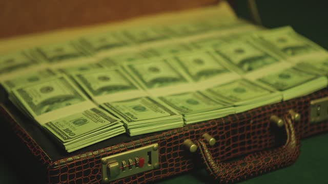 Man opens briefcase full of 100 dollars currency notes in a dimly lit nightclub
