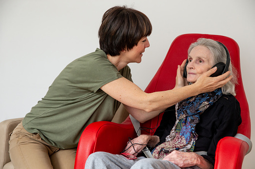Caregiver applying headphones to a senior woman for a music relaxation therapy