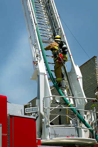 A fireman climbing the ladder of a hook and ladder fire engine.