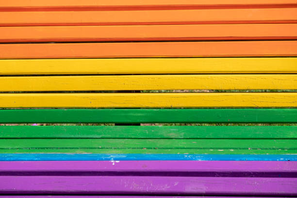Wooden street bench painted in the colours of the rainbow and the LGBTQ flag, Pride Day concept