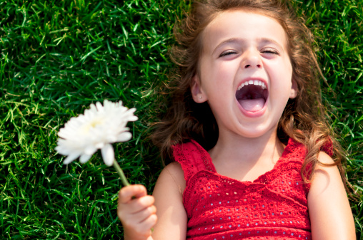 Happy little girl laying on the grass holding a flower