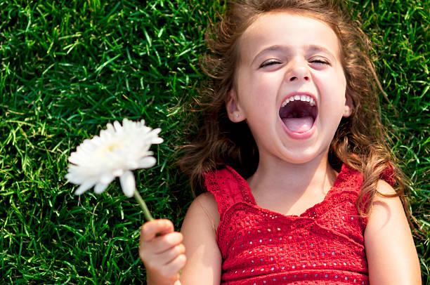 close-up de uma pequena menina sorrindo colocar na grama - child little girls single flower flower - fotografias e filmes do acervo