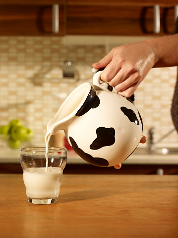 Woman hand Pouring a glass of milk. A glass of fresh milk on the kitchen dining table.