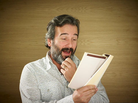 Adults man reading a book. He is influenced by the book he reads and shows different reactions.