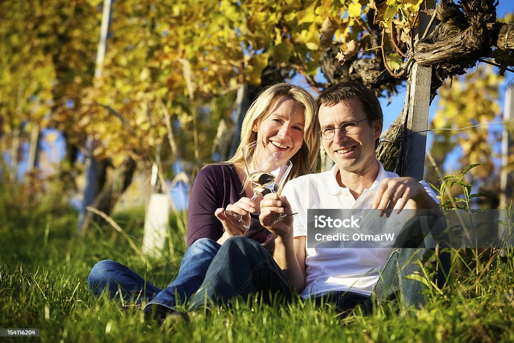 Couple enjoying wine in vineyard. Cheers! Friendly woman and man (couple) sitting in vineyard holding glasses for wine drinking. Celebratory Toast Stock Photo