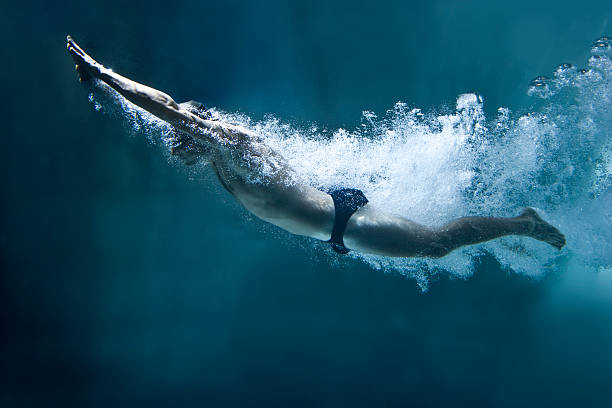 nadador debaixo de água após a saltar sobre fundo azul - swimming male isolated swimming goggles imagens e fotografias de stock