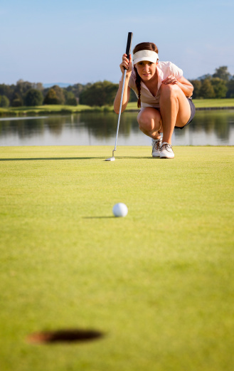 Woman golf player squatting to analyze the green for putting the golf ball into the hole.