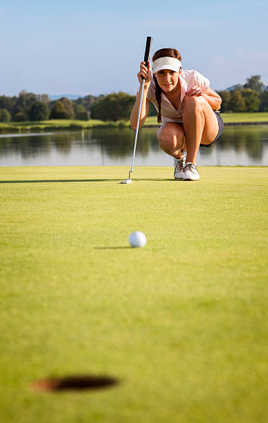 Girl golfer analyzing green for putting ball into cup. Woman golf player squatting to analyze the green for putting the golf ball into the hole. golf concentration stock pictures, royalty-free photos & images
