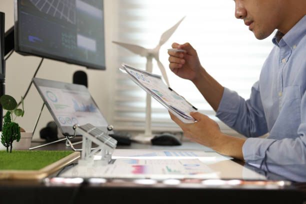 istock Close-up side view of the Mechanical Engineer Designing 3D wind turbine model on a personal computer. Professional working at the office, Concept models of buildings and wind turbines on a desk in the office 1541268441