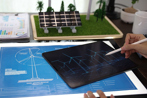 the professional working on a tablet with a black screen mock-up display. Creating a Concept of Wind Turbine and solar panel energy in an Office.