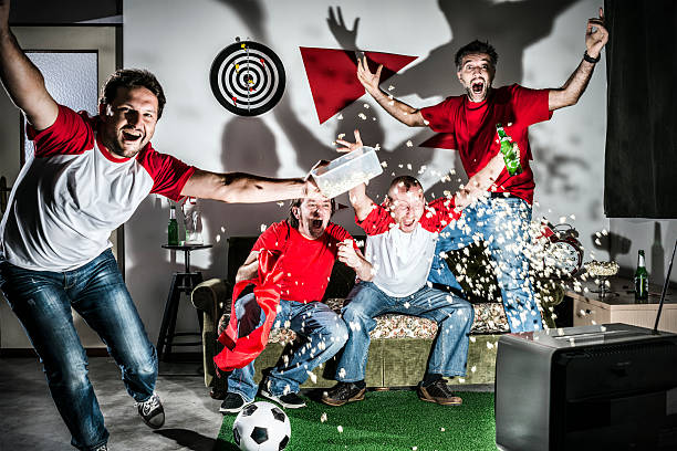 cuatro adultos, hombres jóvenes amigos viendo el fútbol en televisión: objetivo. - cheering men t shirt celebration fotografías e imágenes de stock