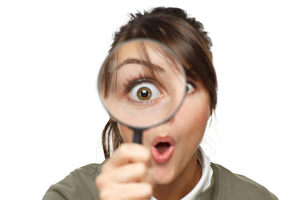 Funny image of young surprised female looking at the camera through a magnifying glass, isolated on white background
