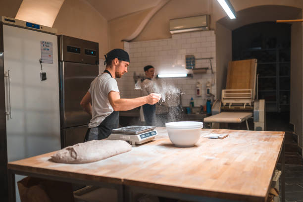 istock Caucasian Baker Sprinkling Flour On A Working Surface In A Bakery 1541333287