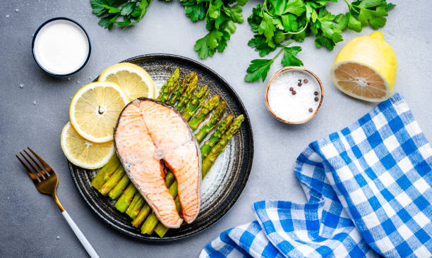 istock Steamed salmon with baked asparagus and lemon on ceramic plate. Grey stone table background, top view 1541343292