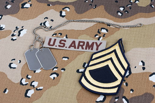 US ARMY Sergeant First Class rank patch and dog tags on desert camouflage uniform background