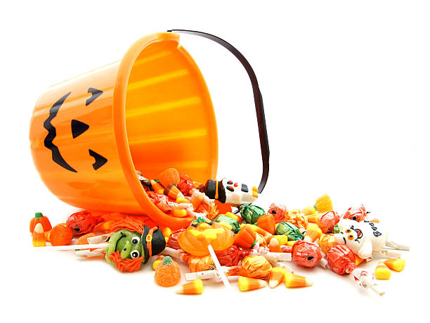 A jack-o-lantern bucket full of candy tipped over  Halloween jack-o-lantern pail with spilling candy over white halloween treats stock pictures, royalty-free photos & images