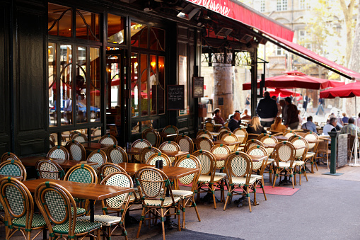 Typical cafe scene in Paris with tables and chairs arranged on the street.  Atmospheric contre jour lighting.  Shallow focus with busy customer area blurred.