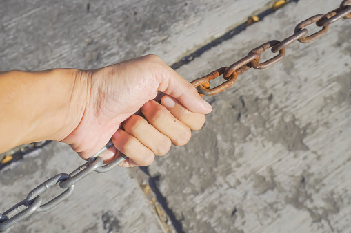 Someone holding a rusty iron chain. Close-up daylight during the day. Concept of strength, mutual assistance, arrest, imprisonment, cumbersome, justice, unity, togetherness, solidarity, inseparable.