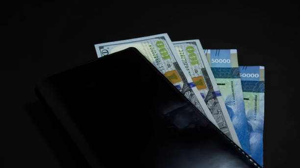 istock Two 100 one hundred dollars banknote bills and two 50 fifty thousand rupiahs inside black long wallet isolated on black dark background 1541438401
