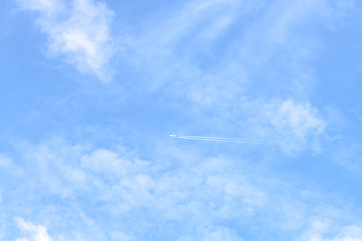 Blue sky, white soft clouds and an airplane with jet stream on an Autumn Day in Australia.