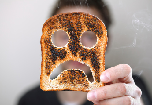 Man holding up a burnt slice of toast with an unhappy smiley conept for bad start to the day