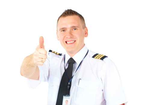 Cheerful airline pilot wearing uniform with epauletes showing thumb up gesture of approval, standing isolated on white background.