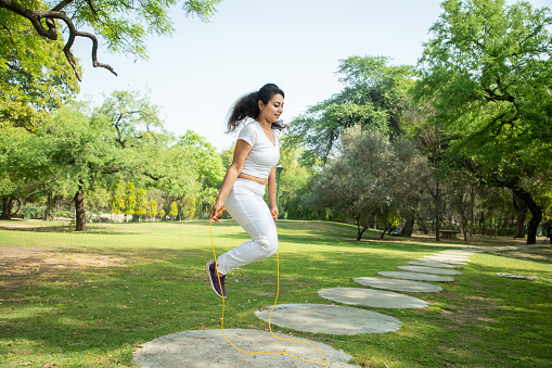 Young indian fitness woman wearing white sportswear skipping rope at park , Asian female Jumping exercise outdoor.