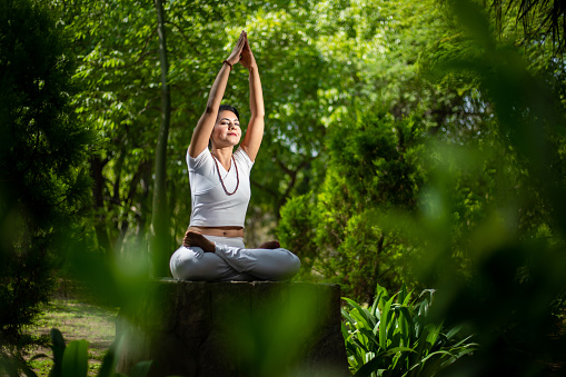 Beautiful indian woman doing yoga exercise while sitting in the green forest nature, Asian female meditation pose, copy space