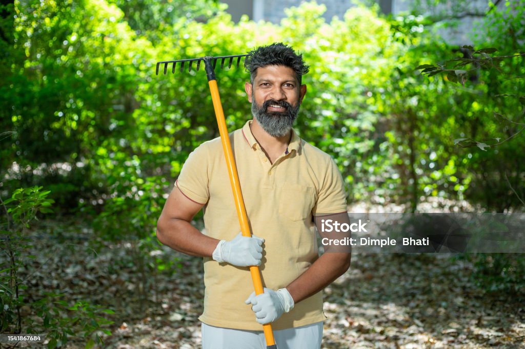 Portrait of happy beard Indian man volunteer holding cleaning equipments to clean fallen leaves in the forest or nature, Spring trash cleaning in park. looking at camera. 35-39 Years Stock Photo