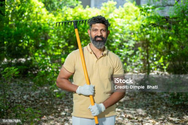 Portrait Of Happy Beard Indian Man Volunteer Holding Cleaning Equipments To Clean Fallen Leaves In The Forest Or Nature Spring Trash Cleaning In Park Looking At Camera Stock Photo - Download Image Now