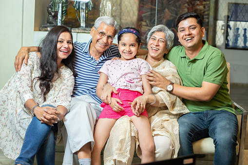 Portrait of happy indian family sitting on sofa at home, Asian grandparents and young parents with girl child.