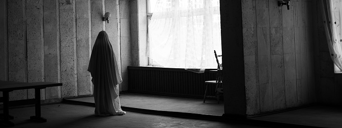 Ghost in abandoned spooky building near windows, horror Halloween concept. Black and white. Banner. Copy space