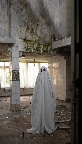 Ghost in a white sheet walking through an abandoned building. Copy space